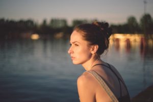 woman thinking intensely as she stands next to a body of water and looks into the distance during dusk