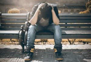 upset man sitting down on a bench holding his head in anguish