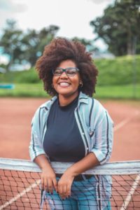 happy woman smiling and leaning against a tennis net