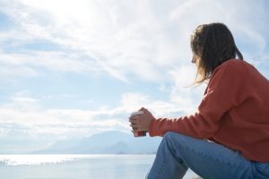 woman thinking as she sits down next to the ocean during a sunny and blue sky day